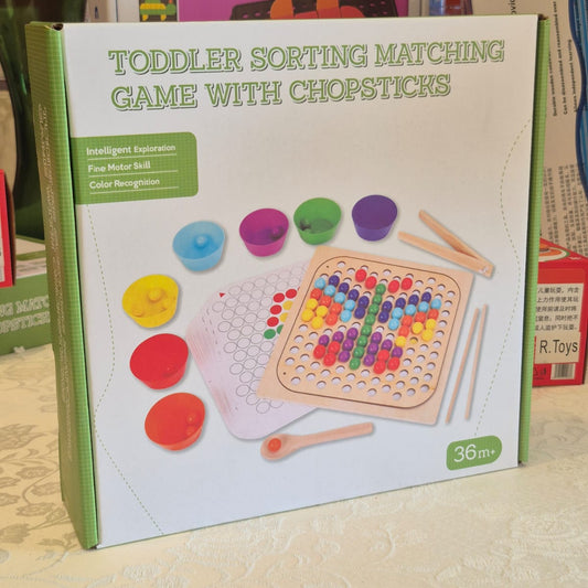 Overhead flat-lay of full sorting game set — wooden pegboard, 7 color cups, beads, and pattern card